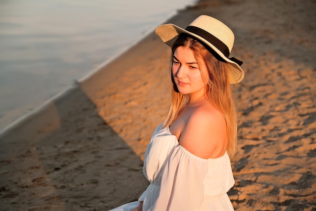 Une belle fille dans un chapeau se tient sur le rivage chapeau à la main