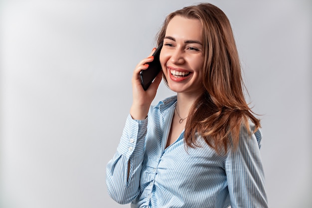 belle fille dans une chemise bleue, parler au téléphone sur fond blanc.