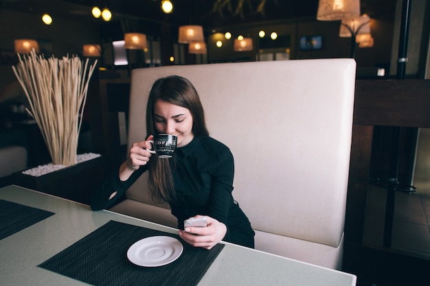 Une belle fille dans une chemise noire, boire du café dans un café