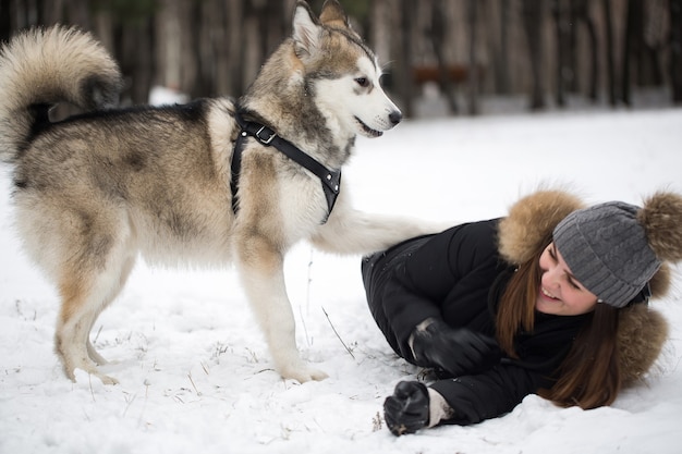 Belle fille dans la forêt d'hiver avec chien. Jouez avec le chien husky sibérien.