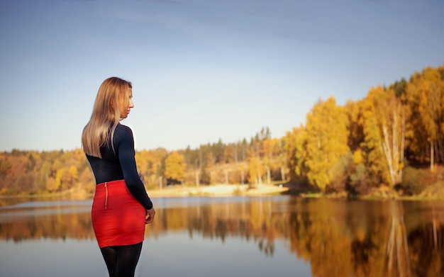 Une belle fille dans une jupe rouge et un T-shirt noir se promène dans un parc d'automne