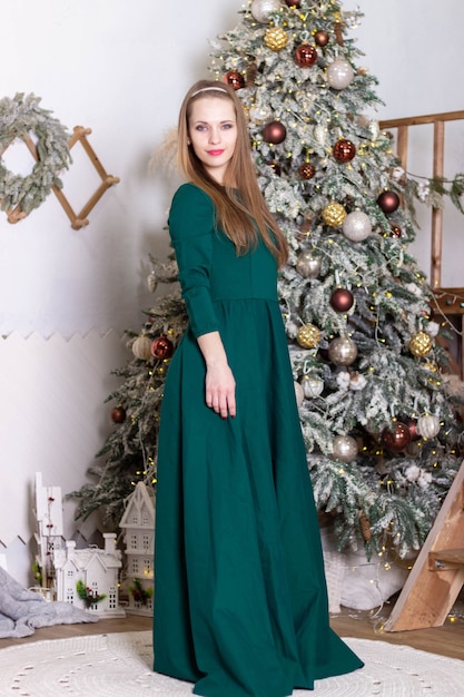 La belle fille dans une longue robe verte se tient près de l'arbre de Noël