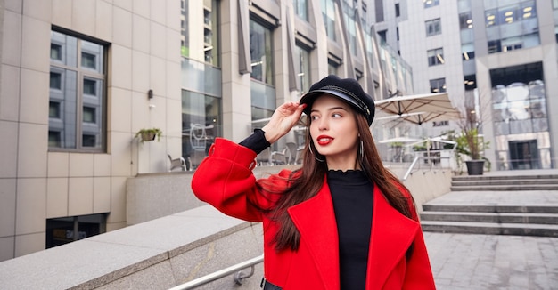 Belle fille dans un manteau rouge et un chapeau noir dans la rue