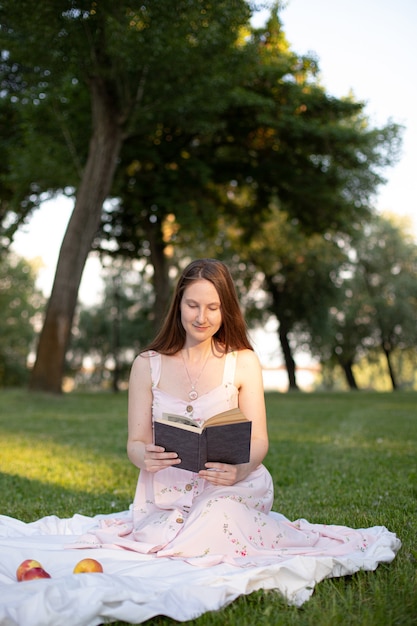 Belle fille dans le parc lit un livre assis sur un tapis