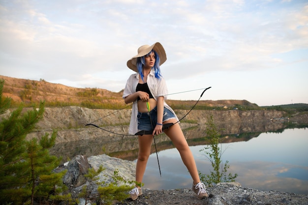 une belle fille dans une perruque bleue et un chapeau de paille avec un arc et une flèche dans les mains