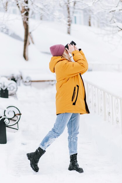 Belle fille dans un photographe de veste jaune prend des photos de neige dans un parc d'hiver