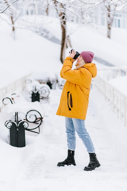 Belle fille dans un photographe de veste jaune prend des photos de neige dans un parc d'hiver