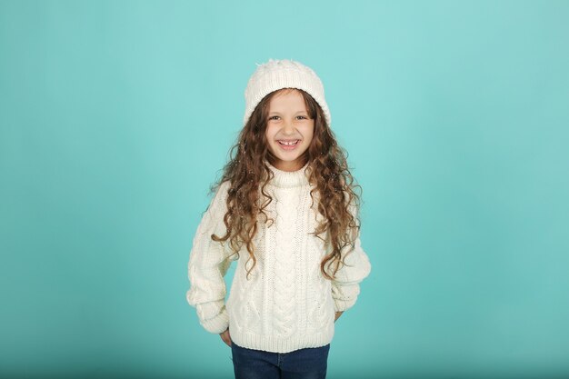 belle fille dans un pull blanc chapeau d'hiver blanc sur fond bleu