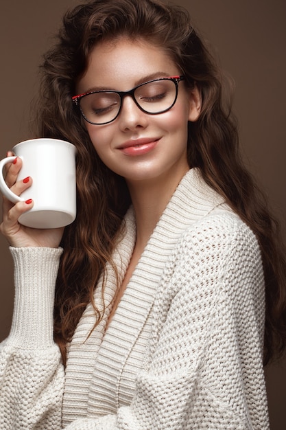 Belle fille dans un pull confortable avec une tasse de thé, des lunettes pour la vision et des lèvres sexy. Beau visage. Photo prise en studio