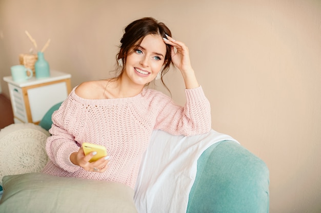 Belle fille dans un pull tricoté tient le téléphone dans sa main et sourit