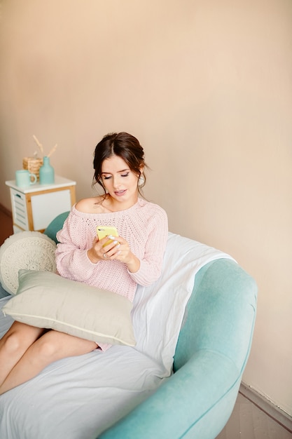 Belle fille dans un pull tricoté tient le téléphone dans sa main et sourit