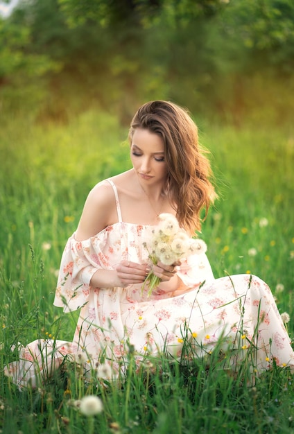 La belle fille dans une robe lumineuse sur le pré rassemble des pissenlits