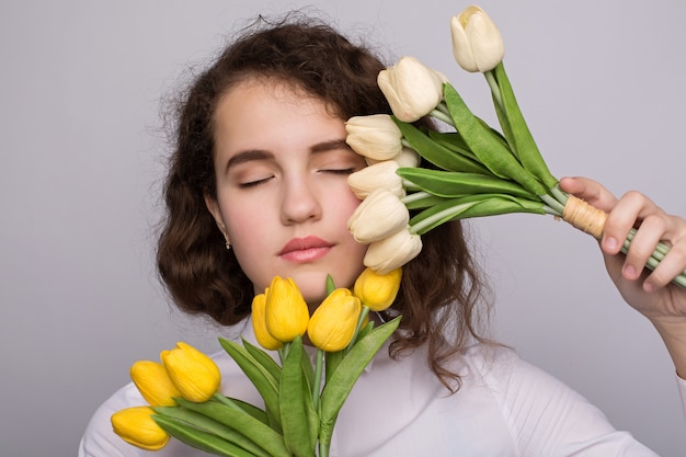 Belle fille dans la robe avec des tulipes fleurs dans les mains sur un fond clair