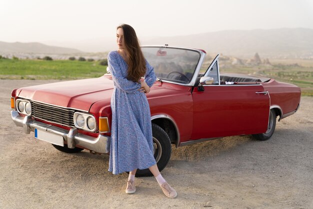 Belle fille dans un style rétro posant près d'une voiture cabriolet rouge vintage