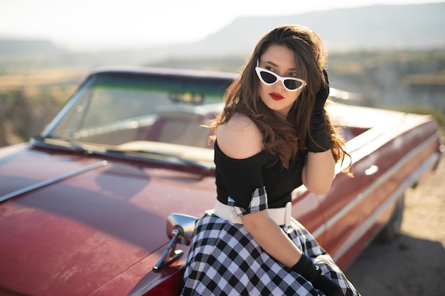 Belle fille dans un style rétro posant près d'une voiture cabriolet rouge vintage