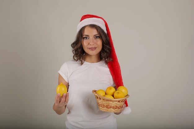 belle fille dans un t-shirt blanc portant un chapeau de père Noël tient un panier de citrons dans ses mains