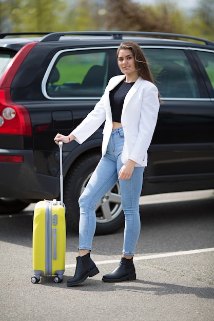 Belle fille dans une veste blanche se dresse avec une grande valise jaune