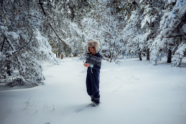 Belle fille debout, en hiver dans le parc forestier, fond de neige d'arbre de Noël, elle se repose dans la station balnéaire. Espace libre pour le texte. Combinaison bleue pour le sport.