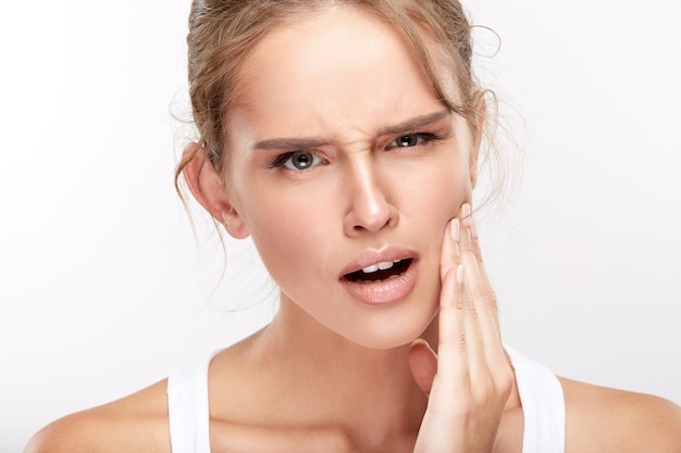 Belle fille avec des dents blanches comme neige sur fond de studio blanc, concept de dentisterie, sourire parfait, douleur, douleur dentaire, regardant la caméra.