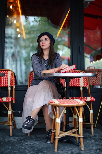 Belle fille élégante à Paris une beauté dans un béret bleu est assise dans un café parisien et boit du café