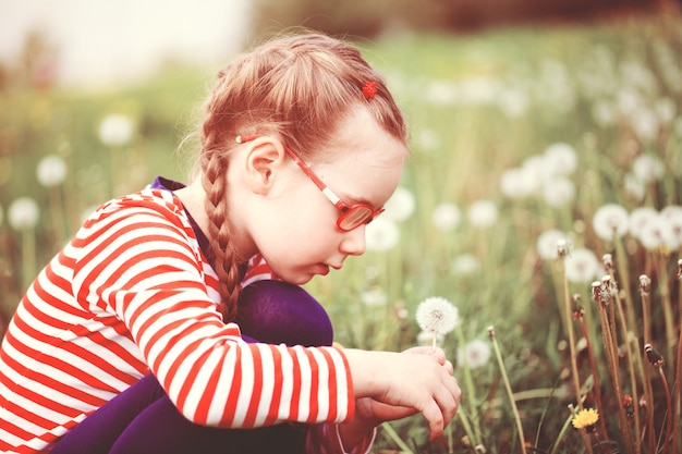 Belle fille émotive avec des lunettes jouant avec des pissenlits. concept d'enfance