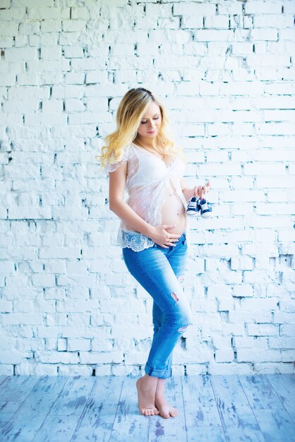 Belle fille enceinte aux cheveux roux avec des baskets pour bébé.