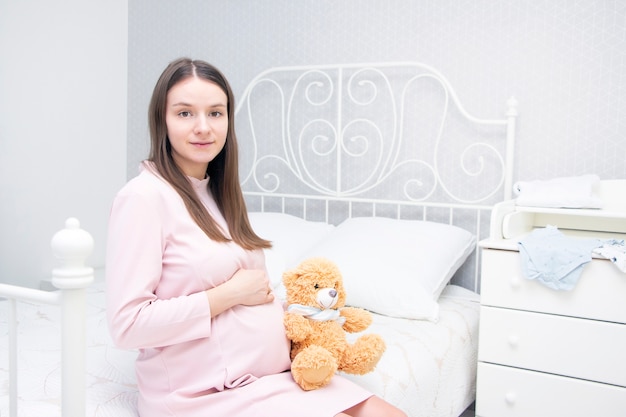 Belle fille enceinte est assise sur le lit et ses mains sont sur son ventre. concept de grossesse, maternité, préparation et attente.