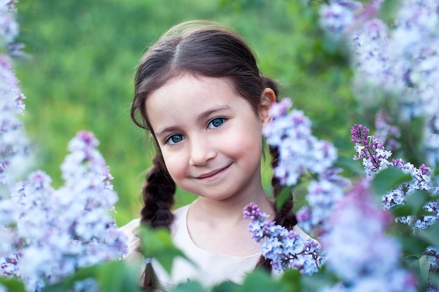 Belle fille enfant souriante dans la robe rose sur le champ de trèfle rouge au coucher du soleil.