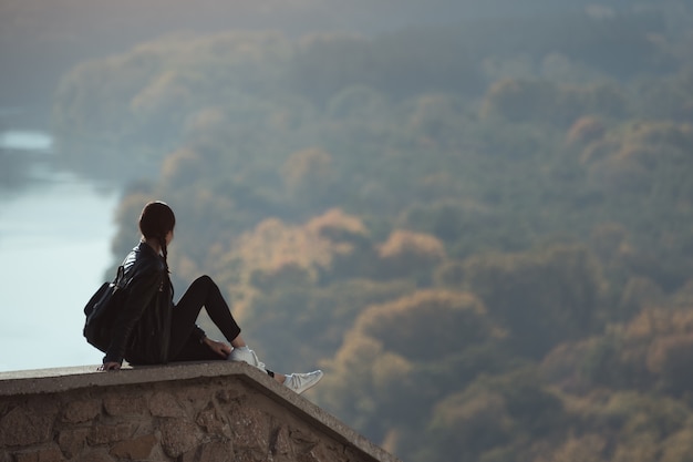 Belle fille est assise sur une colline et regarde au loin. Plaisir de la nature