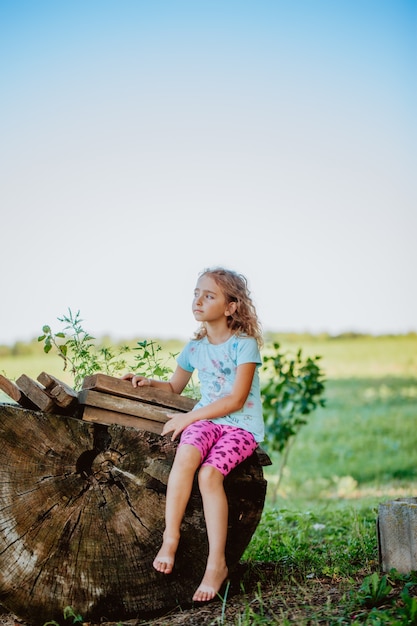 Belle fille est assise sur la grande souche de cabane en rondins.