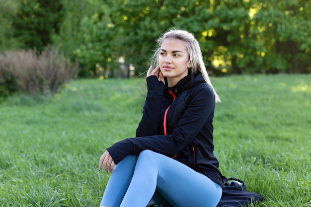 Une belle fille est assise sur l'herbe après une séance d'entraînement Joli modèle en vêtements de sport dans le parc