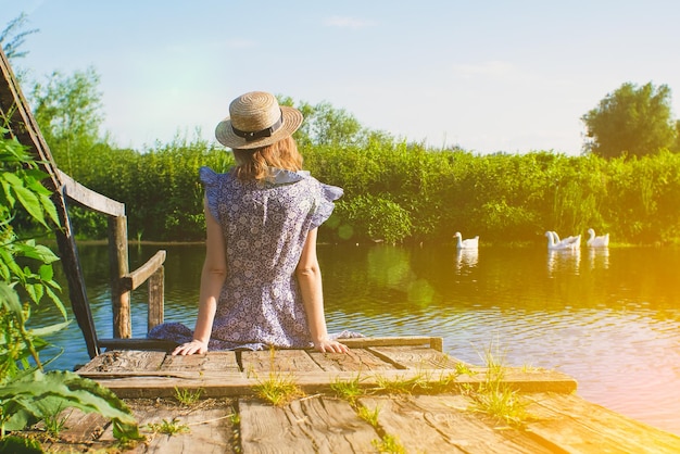 Belle fille est assise sur la jetée en bois Photo rustique et naturelle à l'extérieur Rivière d'été Concept de détente et de voyage