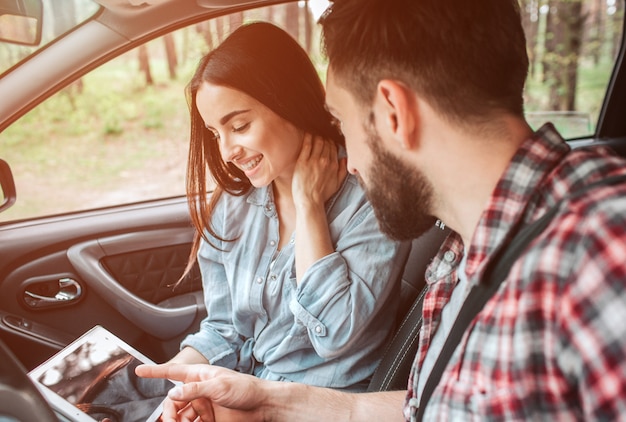 Belle fille est assise avec son petit ami dans la voiture et regarde l'écran. Elle tient la main sur son cou, les yeux fermés et souriant. Elle a l'air heureuse.