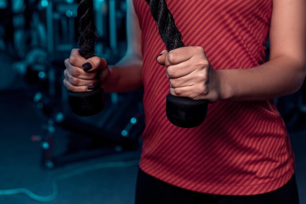 Belle fille faisant des exercices sur le simulateur dans la salle de gym vêtue d'un débardeur rose vierge et de collants. Sur un fond sombre la salle de sport. Habillé en tenue de sport.