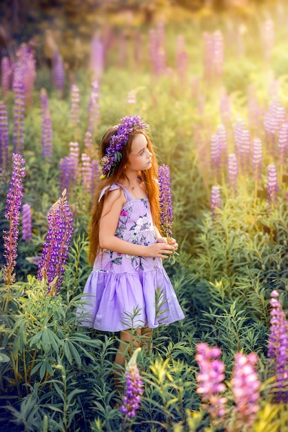 Belle fille avec des fleurs dans les cheveux parmi les fleurs. Photo d'été ensoleillée avec un enfant en fleurs violettes