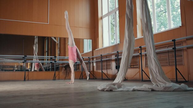 Belle fille flexible s'échauffant au bar de ballet, artiste de cirque