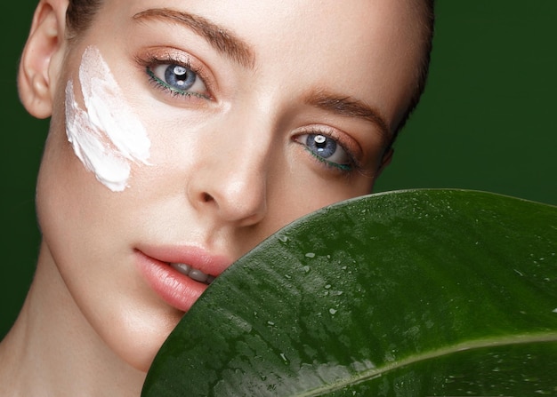 Photo belle fille fraîche avec de la crème cosmétique sur le maquillage naturel du visage et des feuilles vertes