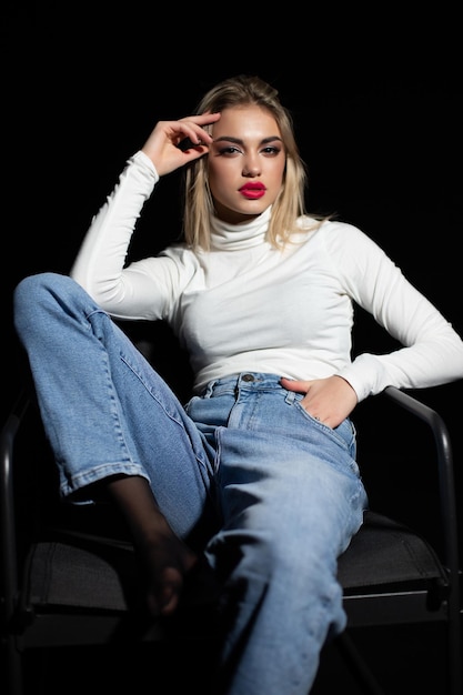 Belle fille en golf blanc et jeans sur fond noir