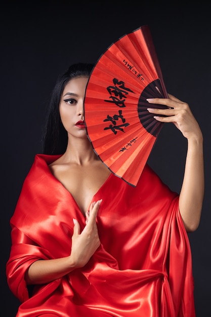 Belle fille habillée en geisha dans un kimono rouge avec un ventilateur