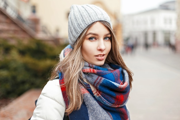 Belle fille heureuse au chapeau et veste blanche avec écharpe sur fond de ville