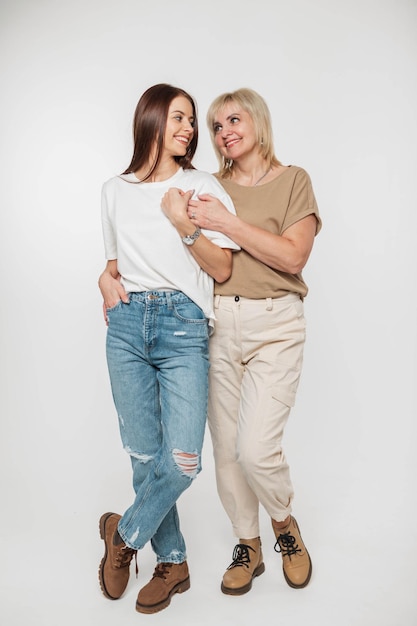 Belle fille heureuse et une femme âgée dans des vêtements en denim à la mode avec un t-shirt jeans et des bottes marron se tiennent debout et s'amusent sur un fond blanc dans le portrait en studio