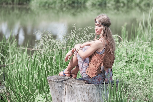 Belle fille hippie assise sur une souche près de l'étang