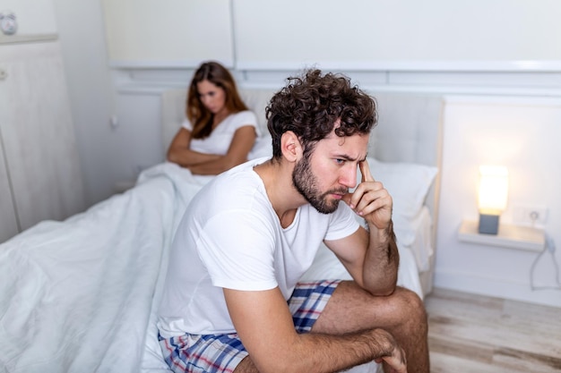 Belle fille et un homme frustré assis dans son lit et ne se regardant pas. Couple bouleversé s'ignorant. Homme inquiet en tension au lit. Jeune couple en colère après un combat.