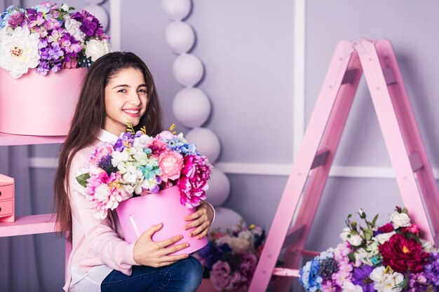 Belle fille en jean et pull rose avec décor de fleurs dans des paniers