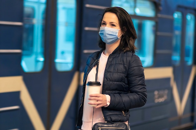 Belle fille, jeune femme debout à la station de métro, métro, métro, en attente des transports publics, train en masque de protection médical sur son visage. Concept de virus pandémique coronavirus. Covid-19