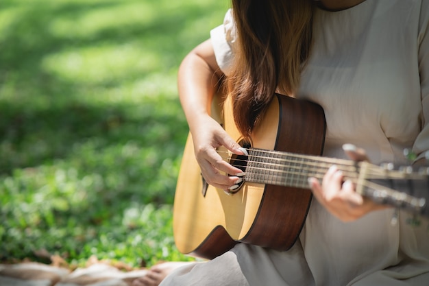 Belle fille jouant de la guitare acoustique dans le jardin