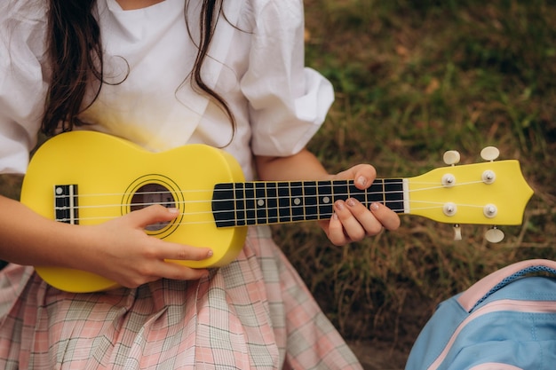 Belle fille jouant de la guitare chantant et souriant joyeusement dans un tissu décontracté avec un chapeau en laine marron musique ou concept de bonheur coucher de soleil effet de ton de lumière chaude Photo de haute qualité