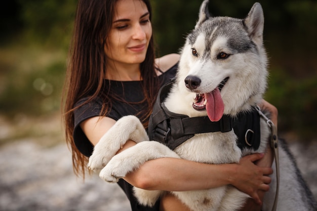 Belle fille joue avec un chien, husky gris et blanc, dans les montagnes au coucher du soleil. Fille indienne et son loup