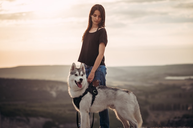 Belle fille joue avec un chien husky gris et blanc dans les montagnes au coucher du soleil