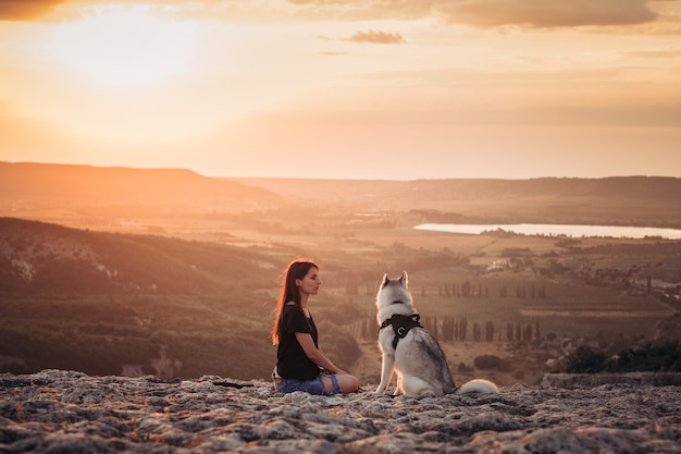 Belle fille joue avec un chien husky gris et blanc dans les montagnes au coucher du soleil